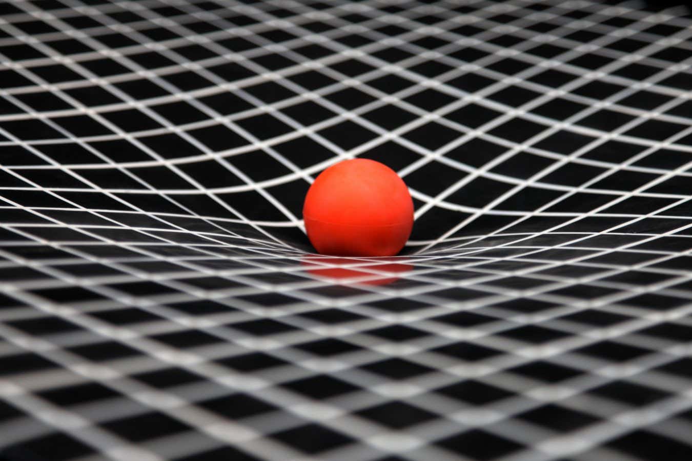 A simulation of gravity showing curved space-time. The ball represents the sun and is resting on a sheet of plastic that stretches under its weight. The curved sheet of plastic demonstrates the way a gravity curves space.