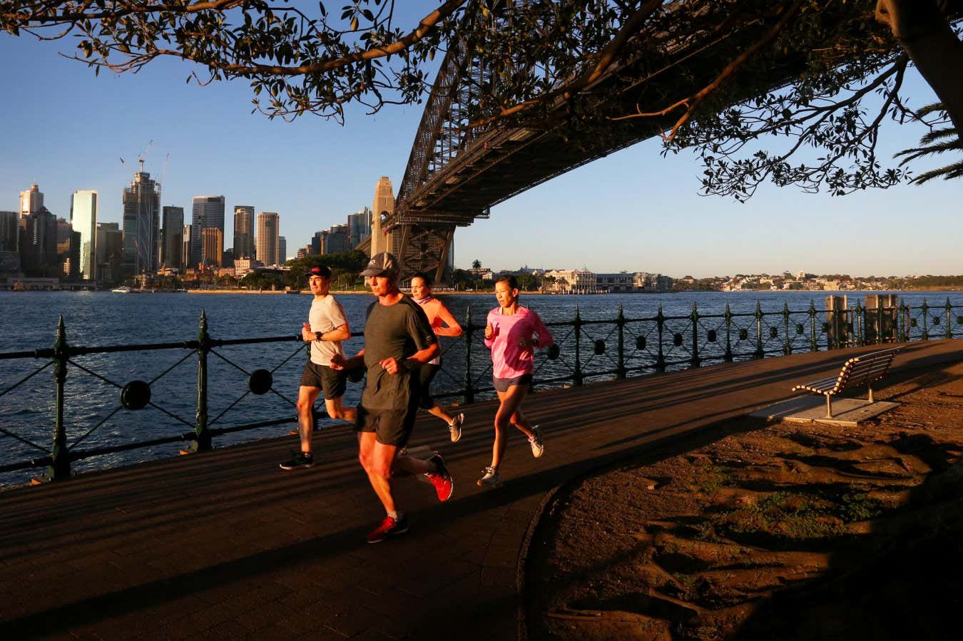 SYDNEY, AUSTRALIA - OCTOBER 06: Joggers move along the Milsons Point boardwalk at sunrise on October 06, 2021 in Sydney, Australia. The NSW government has outlined a roadmap for easing COVID-19 restrictions once the state reaches its 70% double vaccination target - which is expected to be achieved this week. From Monday 11 October restrictions will ease for those who are fully vaccinated, with up to five visitors permitted in a home, and up to 20 people allowed to gather outdoors. Gyms, indoor recreation and sporting facilities able to reopen while retail and hospitality can also reopen subject to density limits. Schools will begin to reopen from 18 October. The 5km rule will be lifted, but residents of Greater Sydney will not be allowed to travel into regional areas until the state reaches 80% double dose vaccinations. (Photo by Lisa Maree Williams/Getty Images)