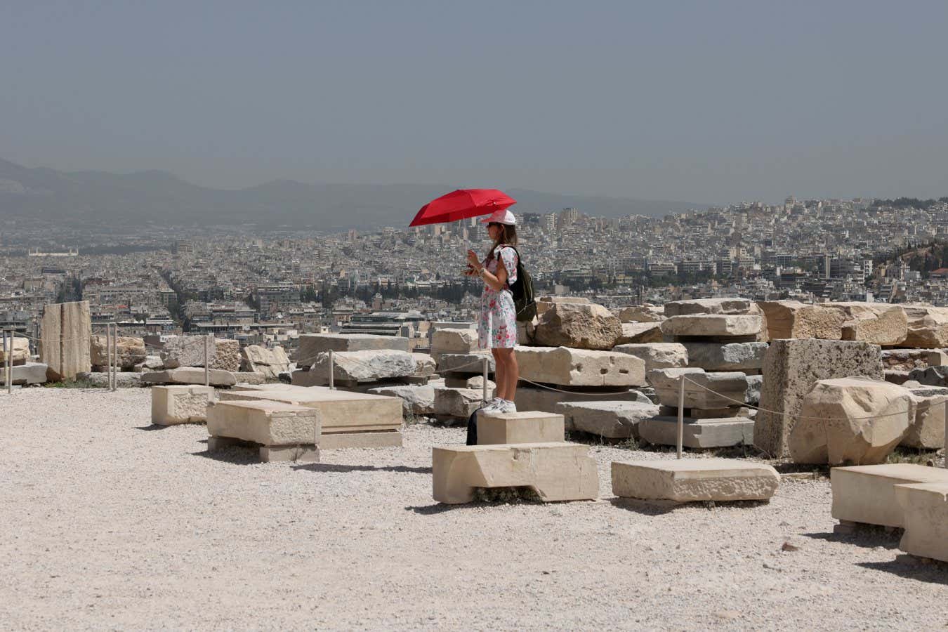 ATHENS, GREECE - JULY 23: A woman use umbrella to protect themselves from the sun as they visit the Parthenon temple atop the Acropolis hill, during a hot weather in Athens, Greece on July 23, 2023. Visits to certain tourist sites, including the Acropolis, home to the Parthenon temple, in Athens, temporarily closed due to a fierce heatwave. (Photo by Costas Baltas/Anadolu Agency via Getty Images)