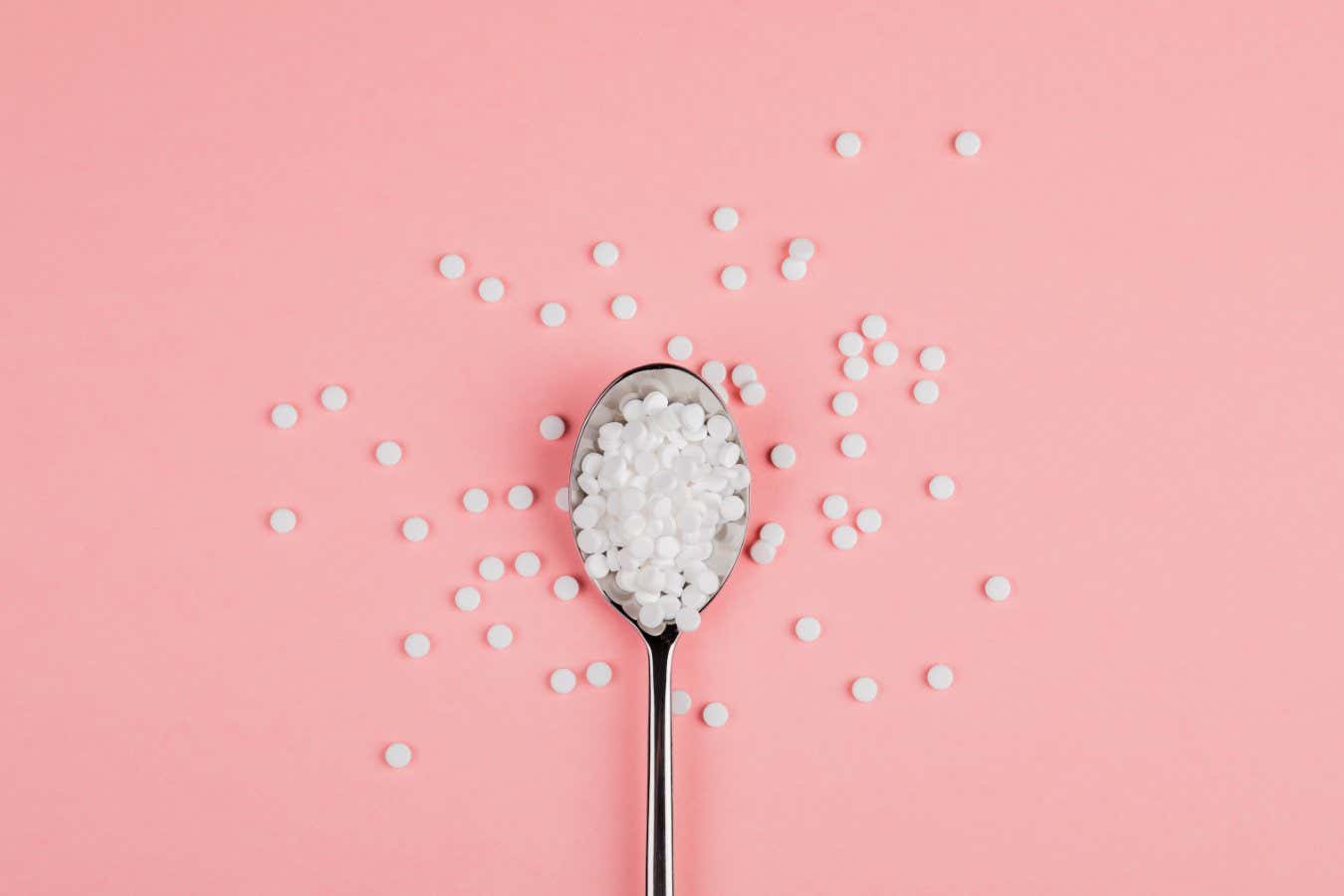Sugar-replacing tablets with a spoon on a pink background.; Shutterstock ID 1326637646; purchase_order: -; job: -; client: -; other: -