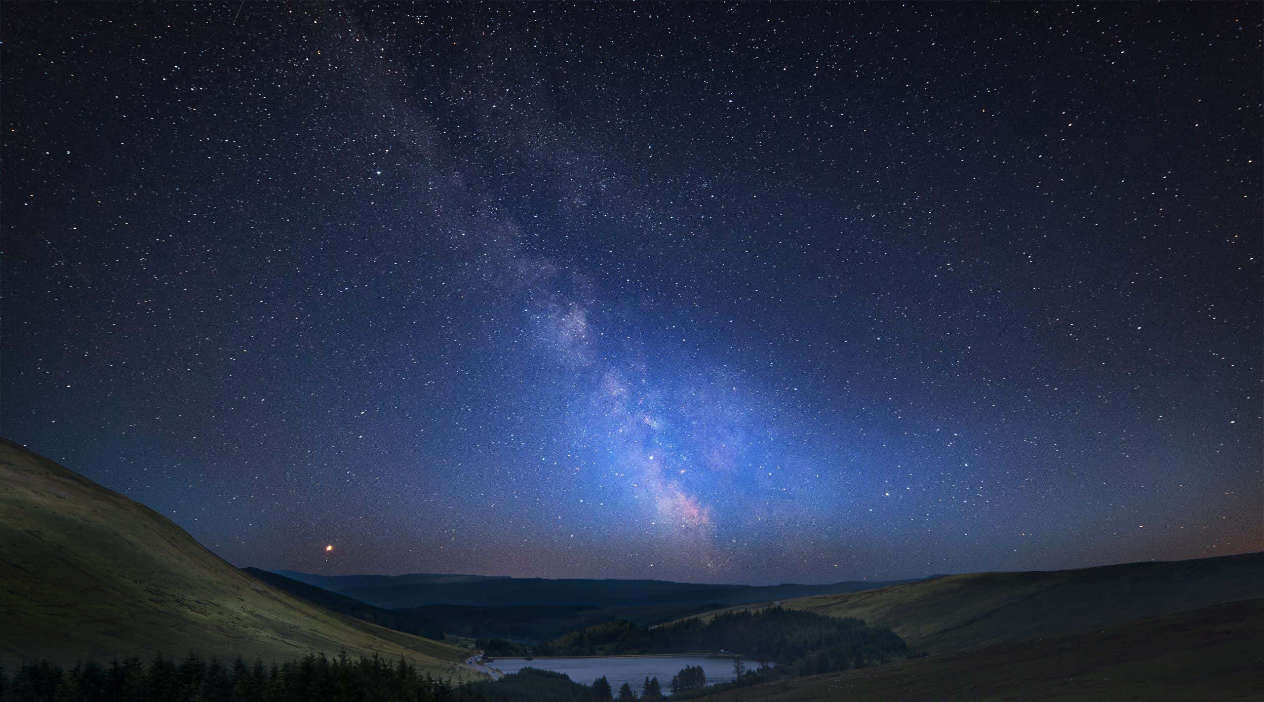 Vibrant Milky Way composite image over landscape of mountains in distance, Brecon Beacons