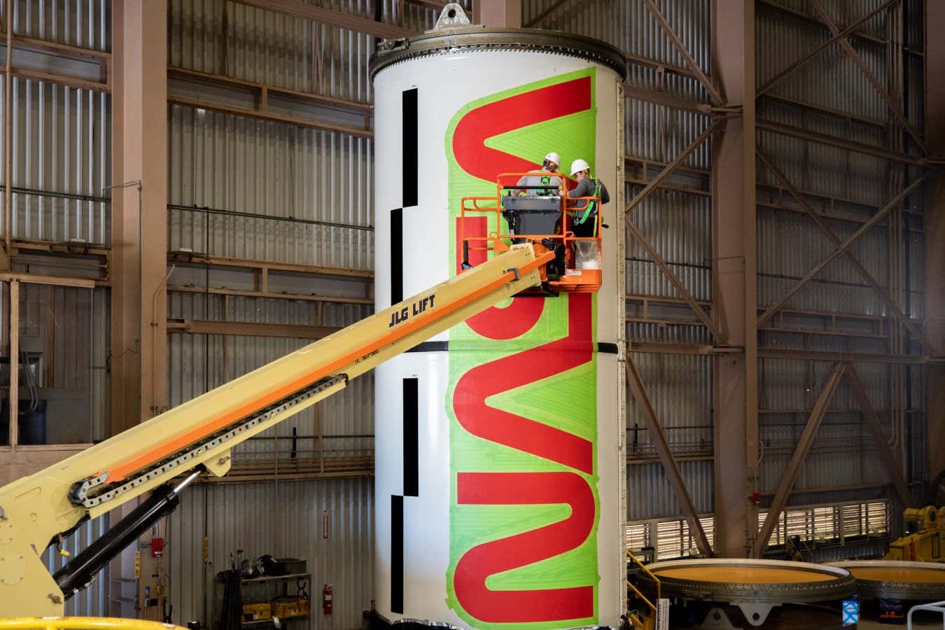 Workers with NASA???s Exploration Ground Systems (EGS) paint the bright red NASA ???worm??? logo on the side of an Artemis II solid rocket booster segment inside the Rotation, Processing and Surge Facility (RPSF) at Kennedy Space Center in Florida on Tuesday, Jan. 30, 2024. The EGS team used a laser projector to mask off the logo with tape, then painted the first coat of the iconic design. The booster segments will help propel the Space Launch System (SLS) rocket on the Artemis II mission to send four astronauts around the Moon as part of the agency???s effort to establish a long-term science and exploration presence at the Moon, and eventually Mars.