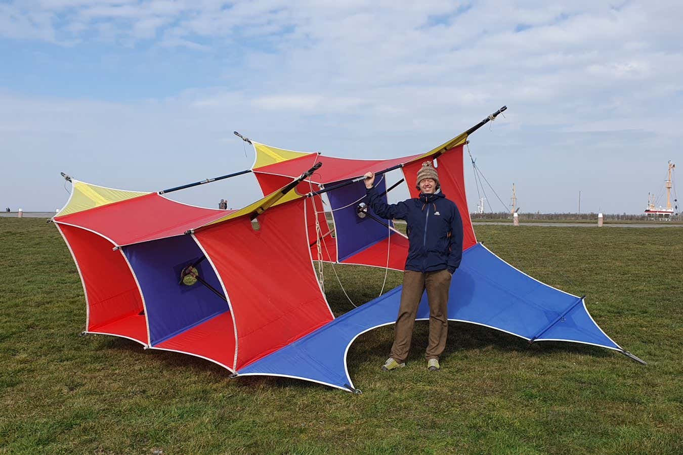 A man standing next to a large red-and-blue kite that will study the total solar eclipse
