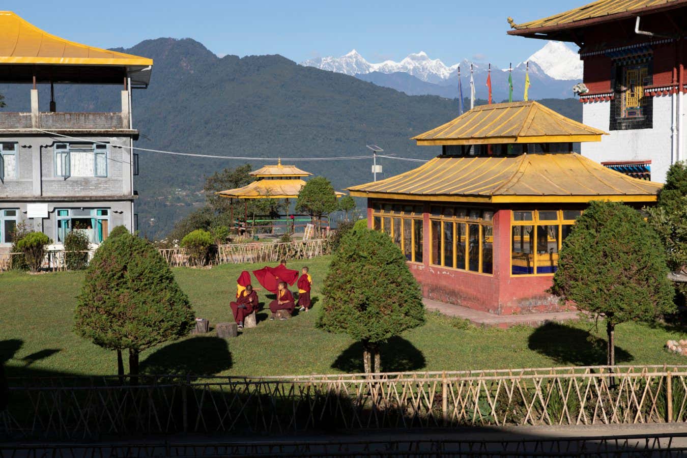 India - Sikkim - Young Buddhist monks in the courtyard of the Tshuklakhang Royal Monastery, one of the oldest monasteries in Sikkim. The Kangchenjunga can be seen in the background (top right). It is the third highest mountain in the world. It rises with an elevation of 8,586 m (28,169 ft) in a section of the Himalayas called Kangchenjunga Himal.
