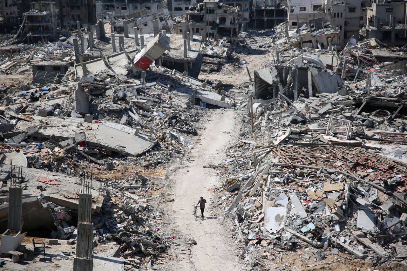 TOPSHOT - A man pushes a bycicle along as he walks amid building rubble in the devastated area around Gaza's Al-Shifa hospital on April 3, 2024, amid the ongoing conflict between Israel and the Palestinian Hamas militant group. (Photo by AFP) (Photo by -/AFP via Getty Images)