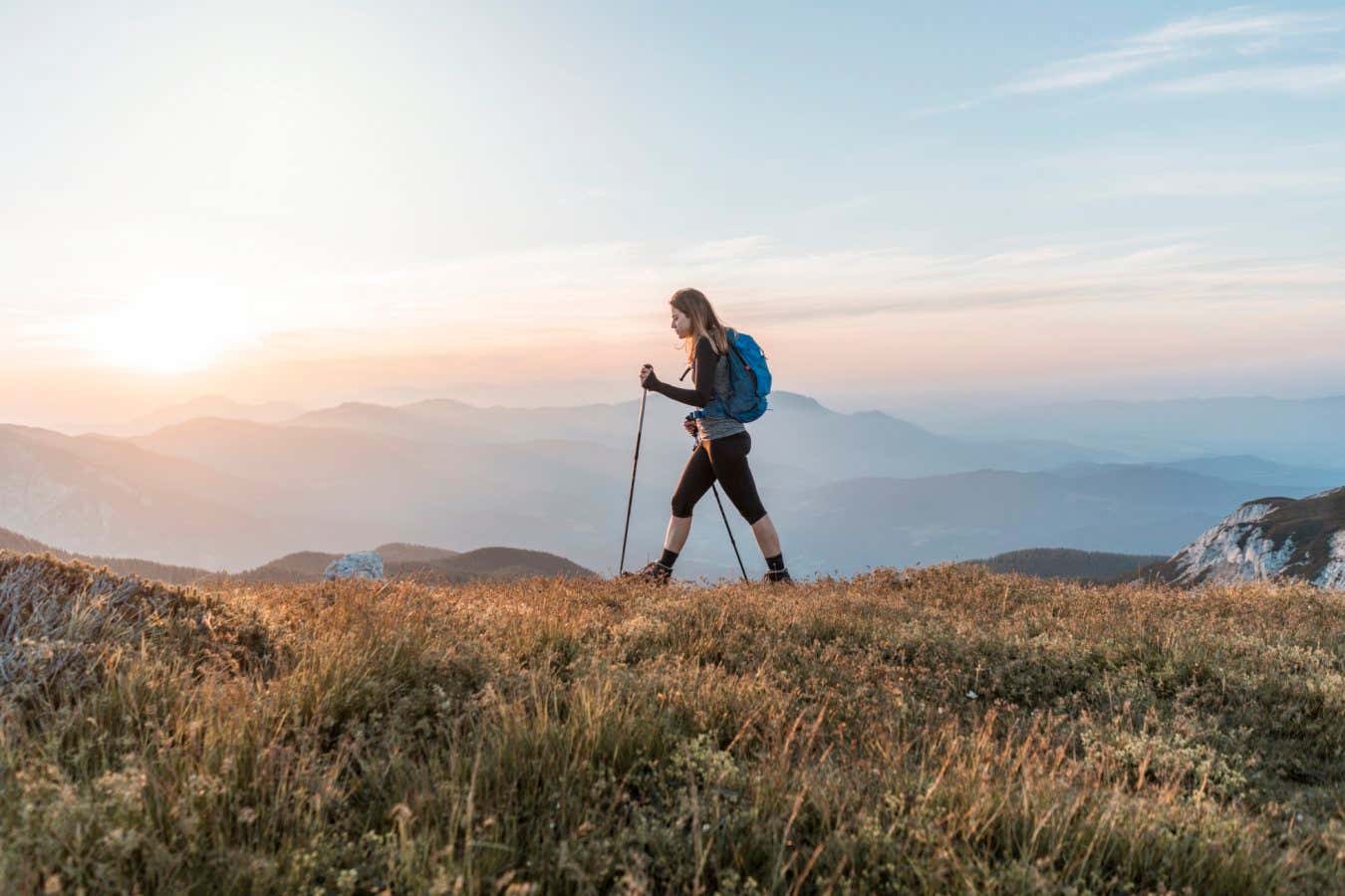 Young woman with a backpack hiking in the mountains. Exploring in the nature, enjoying the view.