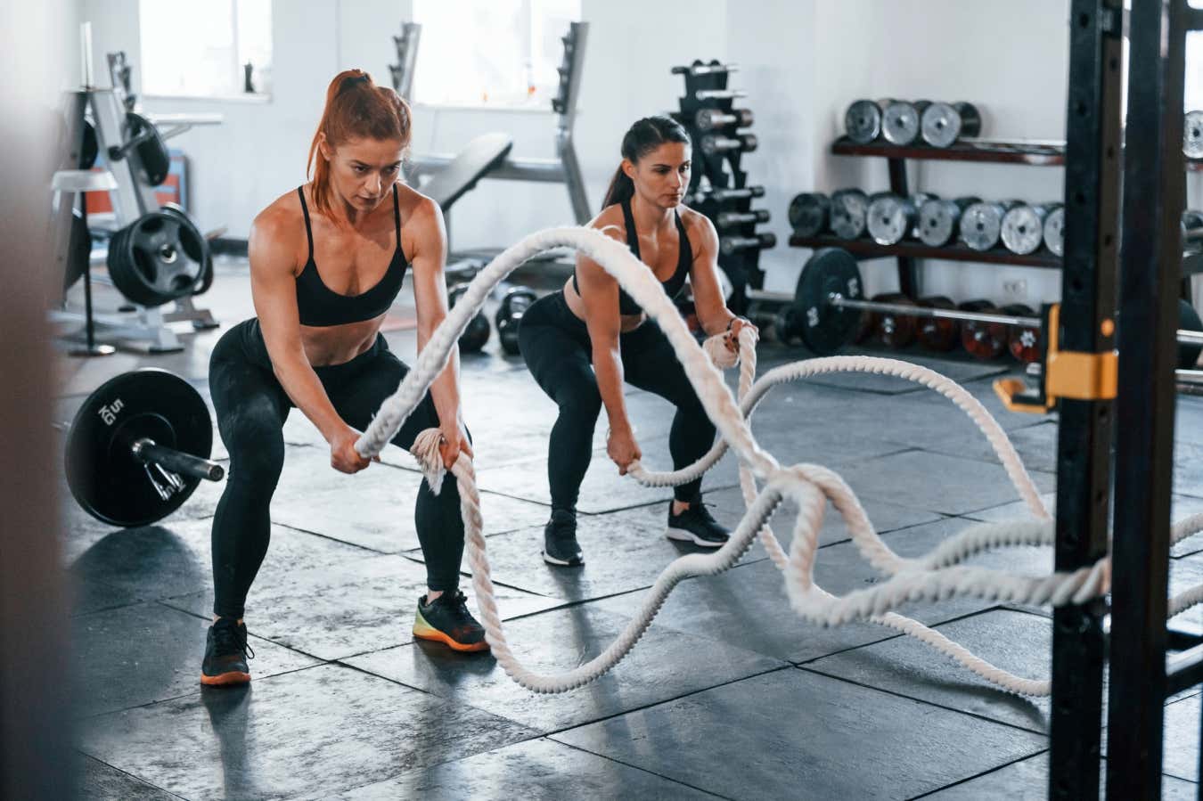 Two women using the battle ropes in the gym
