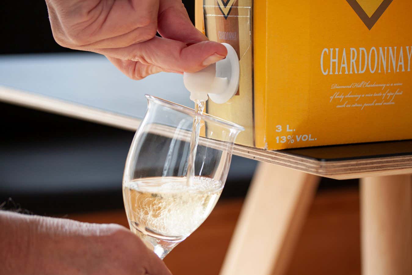 Hand pouring white wine into a glass from a BIB - cardboard bag in box with open tap standing on a table. Close up image. Copenhagen, Denmark - November 2, 2022. ; Shutterstock ID 2221452919; purchase_order: -; job: -; client: -; other: -